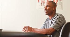 man with shaved head in gray short sleeve shirt sitting at desk